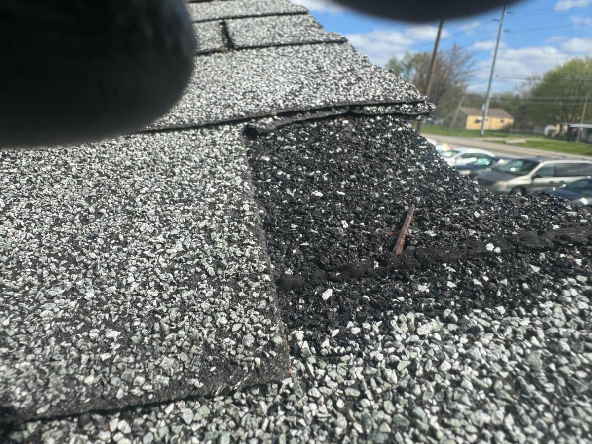 Displaced ridge shingle with an exposed fastener and heavy granule loss