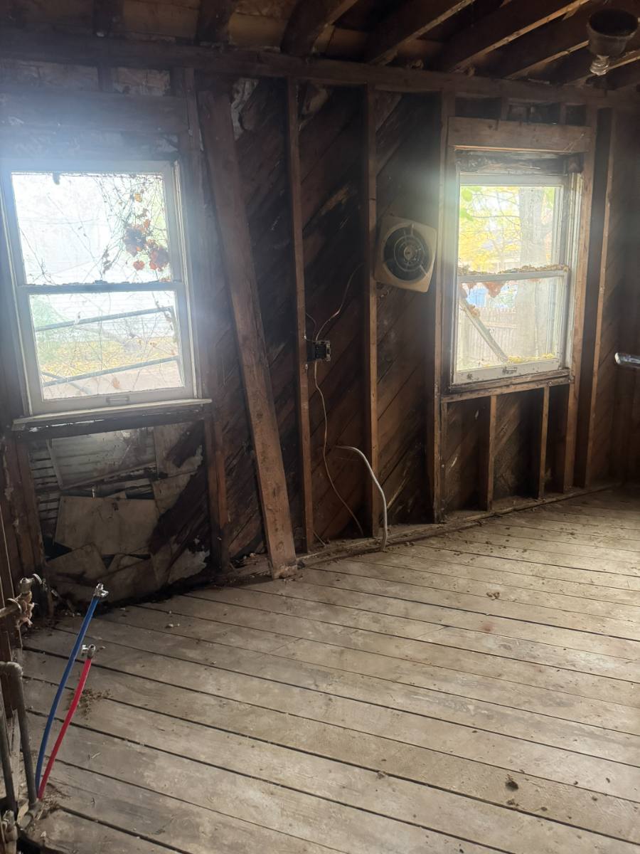 Bathroom demolished to studs and subfloor with charred framing, exposed diagonal sheathing and abandoned wiring